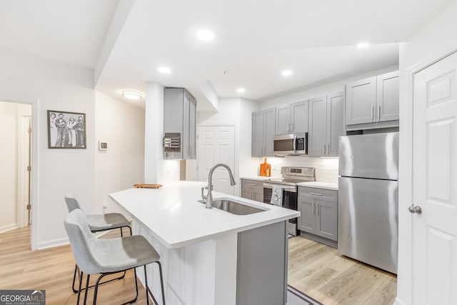 kitchen featuring appliances with stainless steel finishes, a kitchen breakfast bar, gray cabinets, light countertops, and a sink