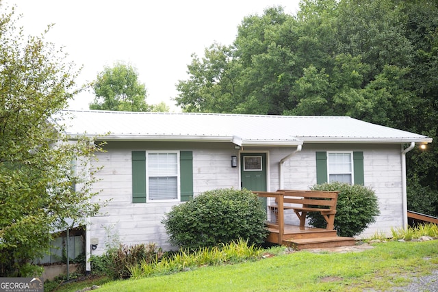 ranch-style home with a front yard, metal roof, and a wooden deck