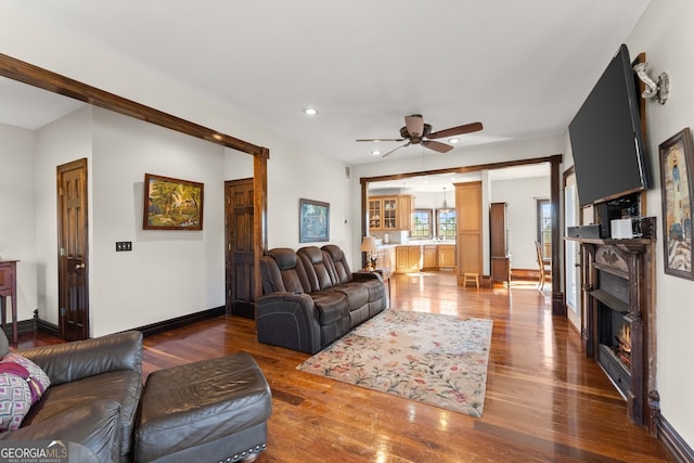 living room featuring a warm lit fireplace, recessed lighting, wood finished floors, a ceiling fan, and baseboards