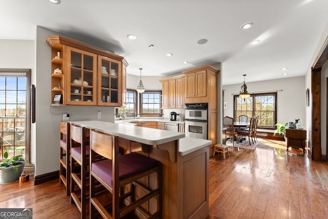 kitchen featuring appliances with stainless steel finishes, glass insert cabinets, decorative light fixtures, a peninsula, and light countertops