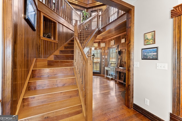 stairs with a high ceiling, wood walls, wood finished floors, and baseboards