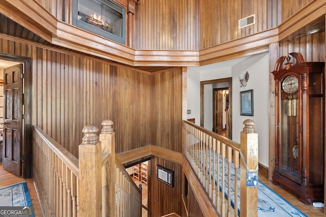 hall with visible vents, wood walls, a towering ceiling, and an upstairs landing