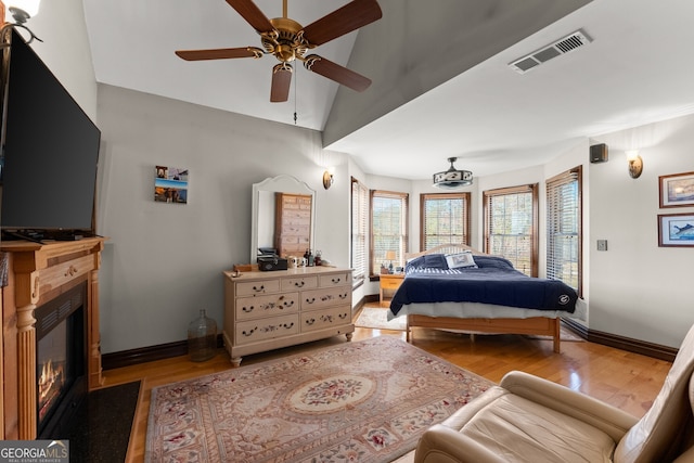 bedroom featuring visible vents, a glass covered fireplace, vaulted ceiling, wood finished floors, and baseboards