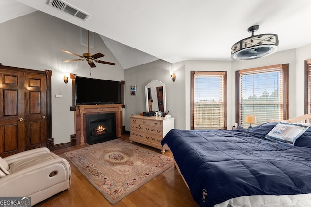 bedroom with visible vents, a fireplace with flush hearth, vaulted ceiling, ceiling fan, and wood finished floors