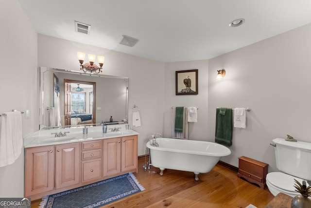 bathroom featuring visible vents, toilet, a sink, wood finished floors, and a freestanding tub