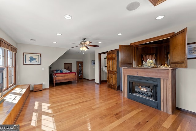 bedroom with a warm lit fireplace, visible vents, light wood-style flooring, and multiple windows