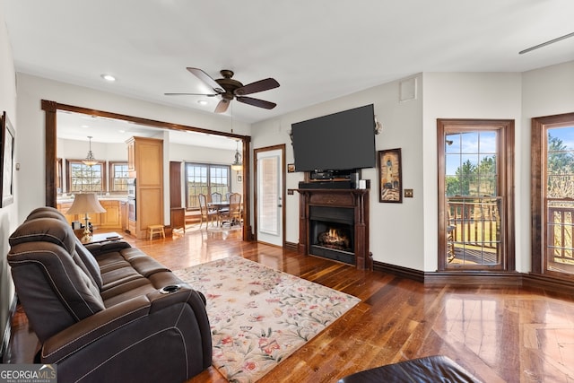 living room featuring dark wood-style floors, recessed lighting, a ceiling fan, a warm lit fireplace, and baseboards