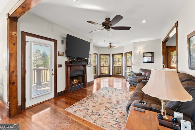 living room with a ceiling fan, a lit fireplace, baseboards, and wood finished floors