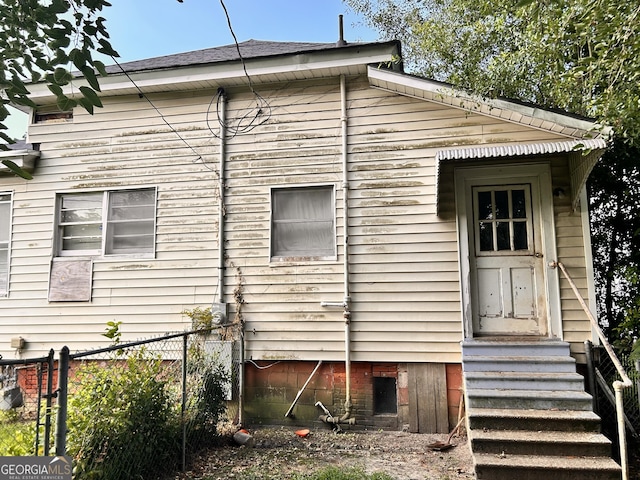 rear view of house featuring entry steps and fence