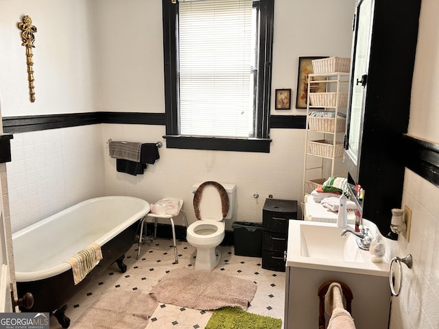 bathroom featuring a wainscoted wall, tile walls, a freestanding bath, toilet, and vanity