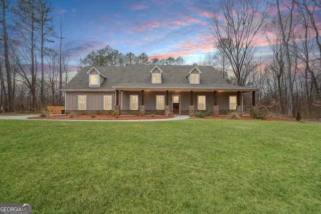 view of front of property with board and batten siding, covered porch, a yard, and a shingled roof