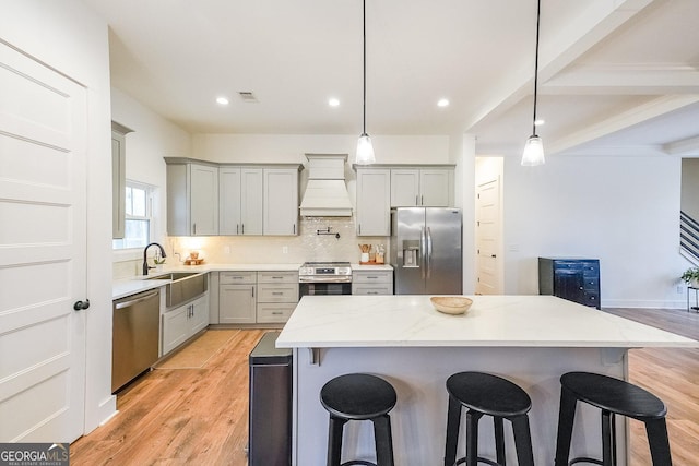 kitchen with a kitchen bar, custom range hood, appliances with stainless steel finishes, and light wood-style flooring