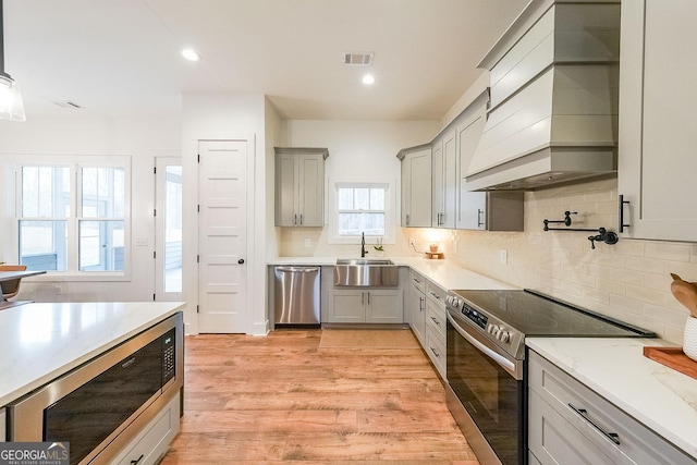 kitchen with light wood finished floors, visible vents, custom range hood, appliances with stainless steel finishes, and a sink