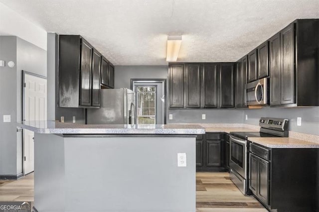 kitchen with light wood finished floors, appliances with stainless steel finishes, light countertops, and a textured ceiling