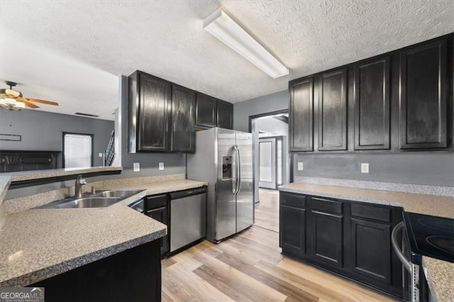 kitchen with light wood-style flooring, stainless steel appliances, dark cabinetry, light countertops, and a sink