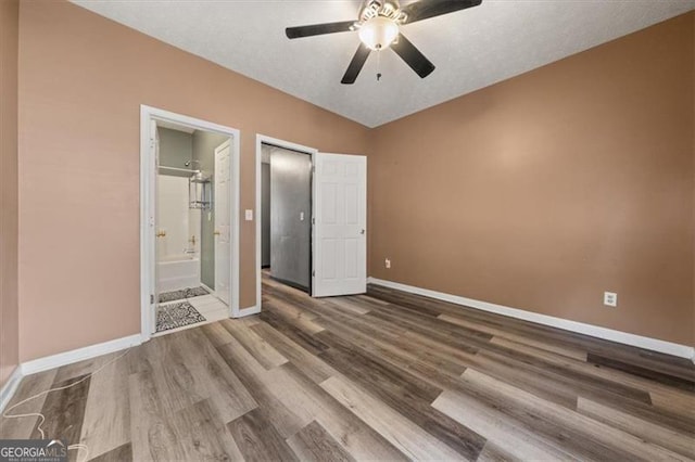 unfurnished bedroom featuring ensuite bathroom, ceiling fan, wood finished floors, and baseboards