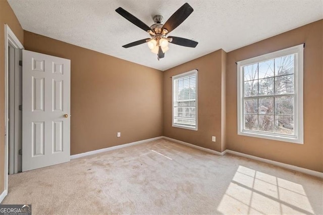 spare room with a textured ceiling, baseboards, and light colored carpet