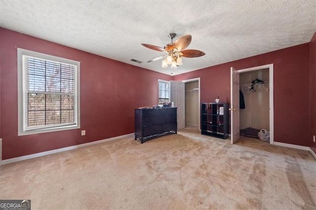 unfurnished bedroom with a textured ceiling, light colored carpet, visible vents, baseboards, and multiple closets