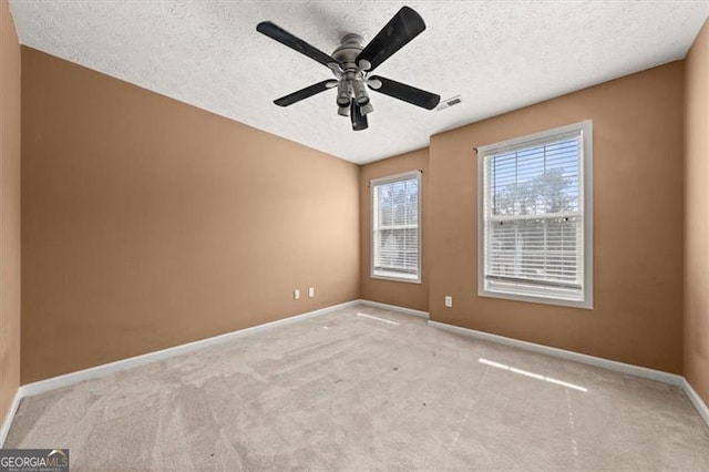 spare room with a textured ceiling, a ceiling fan, visible vents, and baseboards