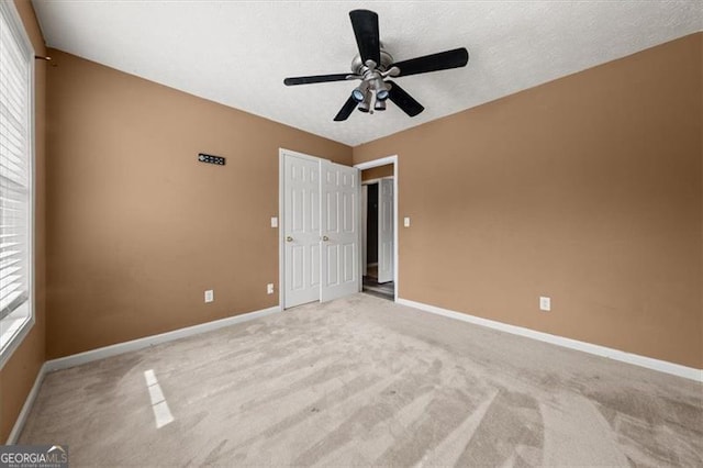 unfurnished bedroom featuring ceiling fan, baseboards, a textured ceiling, and light colored carpet