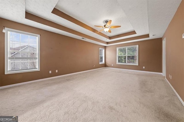 carpeted spare room with a tray ceiling, ceiling fan, a textured ceiling, and baseboards