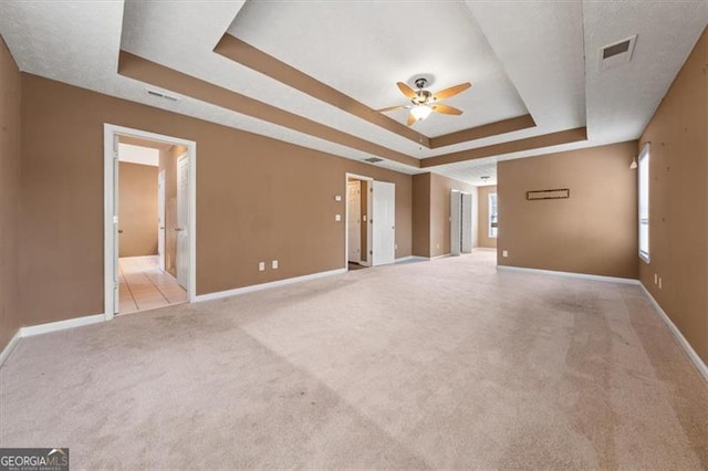 interior space featuring a tray ceiling, visible vents, a ceiling fan, light carpet, and baseboards