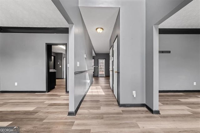 hall featuring baseboards, light wood-style flooring, and a textured ceiling