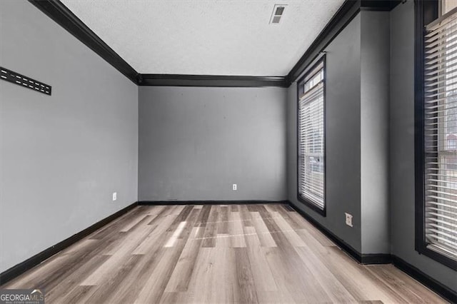 empty room featuring light wood-style floors, a textured ceiling, baseboards, and crown molding