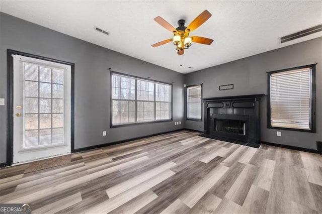 unfurnished living room with light wood finished floors, baseboards, visible vents, a tile fireplace, and a textured ceiling