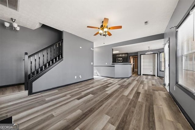 unfurnished living room featuring visible vents, baseboards, a ceiling fan, stairway, and wood finished floors