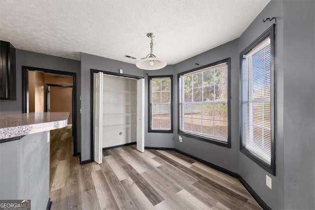 unfurnished dining area with baseboards, a textured ceiling, visible vents, and light wood-style floors