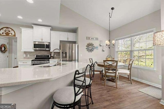 kitchen featuring lofted ceiling, appliances with stainless steel finishes, white cabinetry, a sink, and wood finished floors