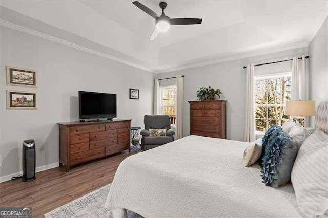 bedroom with ornamental molding, a tray ceiling, baseboards, and wood finished floors