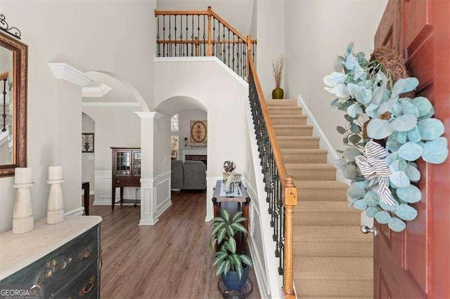 entrance foyer featuring stairs, arched walkways, a high ceiling, and wood finished floors