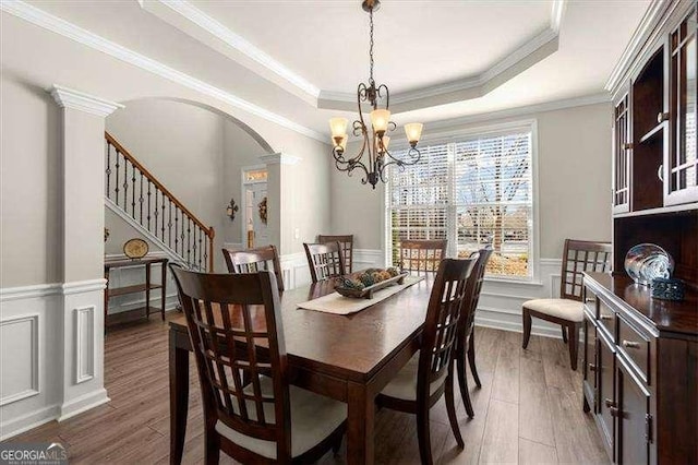 dining room featuring arched walkways, a wainscoted wall, a raised ceiling, a decorative wall, and wood finished floors