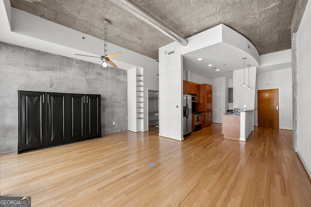 unfurnished living room featuring a towering ceiling, light wood-style flooring, and ceiling fan