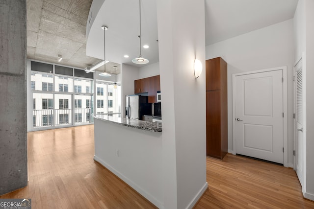 kitchen featuring baseboards, light wood-style flooring, dark stone countertops, hanging light fixtures, and stainless steel refrigerator with ice dispenser