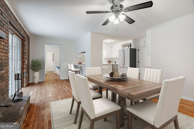 dining room featuring ceiling fan, brick wall, light wood-type flooring, and baseboards