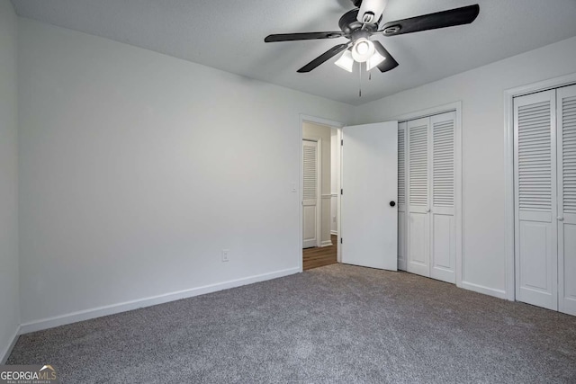 unfurnished bedroom featuring baseboards, dark carpet, a ceiling fan, and multiple closets