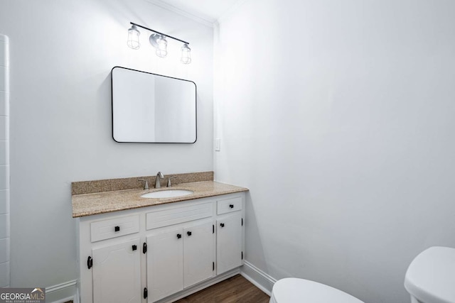 bathroom featuring toilet, ornamental molding, vanity, wood finished floors, and baseboards