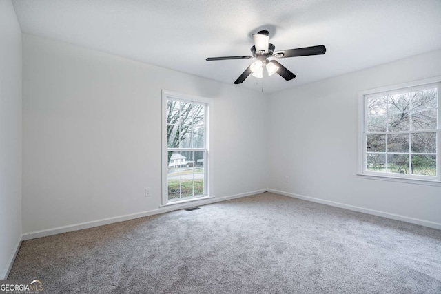 empty room with visible vents, carpet floors, a ceiling fan, and baseboards