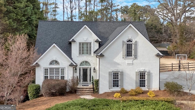 view of front of property with a shingled roof, fence, and stucco siding