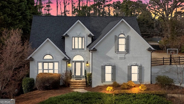 french country inspired facade featuring a shingled roof, fence, and stucco siding