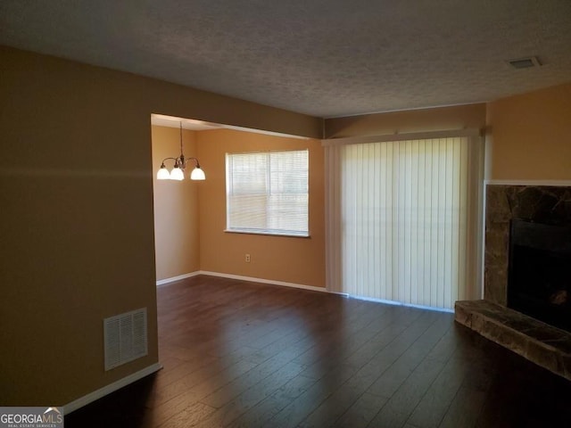 unfurnished living room featuring a textured ceiling, a stone fireplace, a notable chandelier, wood finished floors, and visible vents