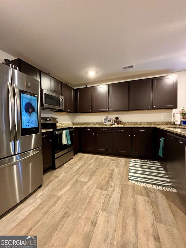 kitchen with light stone counters, light wood-style flooring, dark brown cabinetry, stainless steel appliances, and visible vents