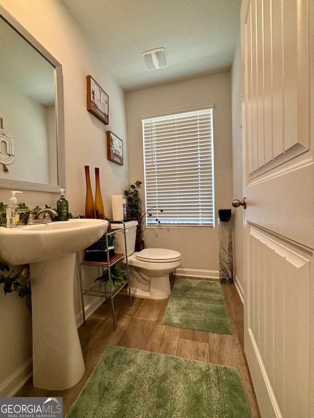 bathroom featuring toilet, a sink, wood finished floors, visible vents, and baseboards