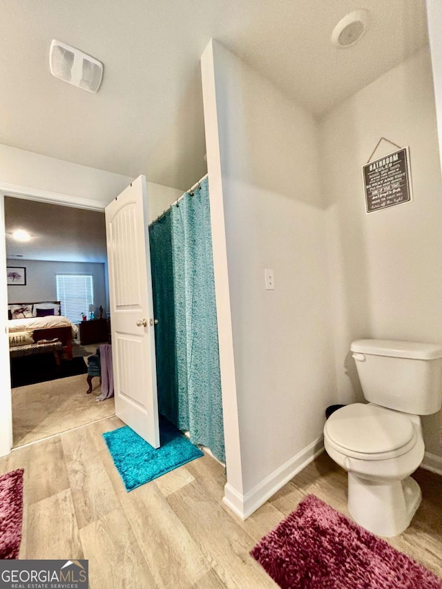 ensuite bathroom featuring baseboards, visible vents, toilet, wood finished floors, and ensuite bathroom