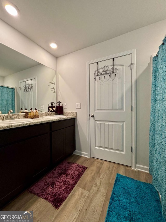 bathroom featuring double vanity, a sink, baseboards, and wood finished floors