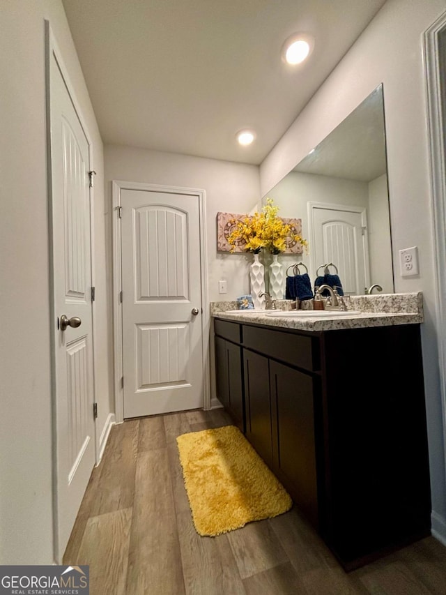 full bathroom with recessed lighting, double vanity, a sink, and wood finished floors