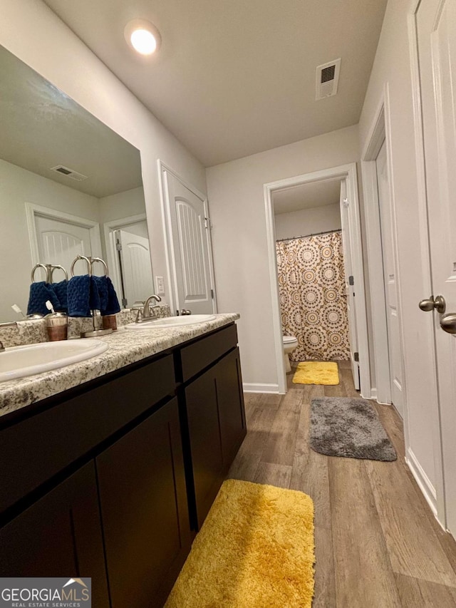 bathroom featuring double vanity, visible vents, toilet, and wood finished floors